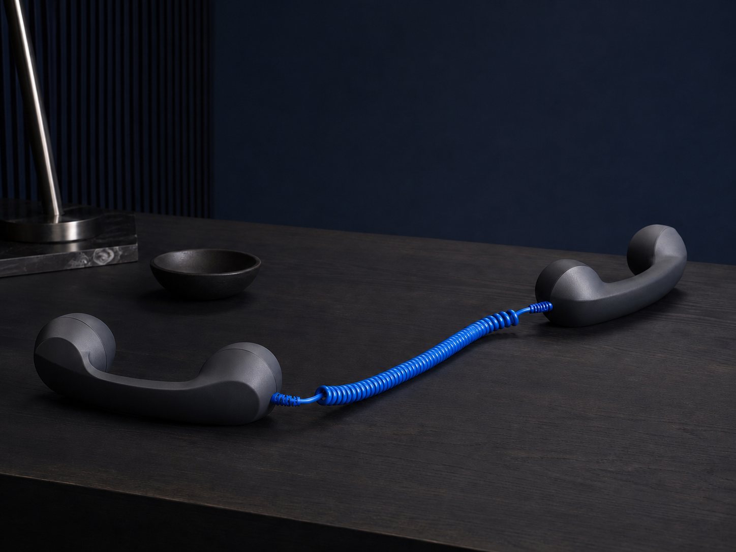 Zwei Telefonhörer auf einem dunklen Tisch, verbunden durch ein blaues Spiralkabel